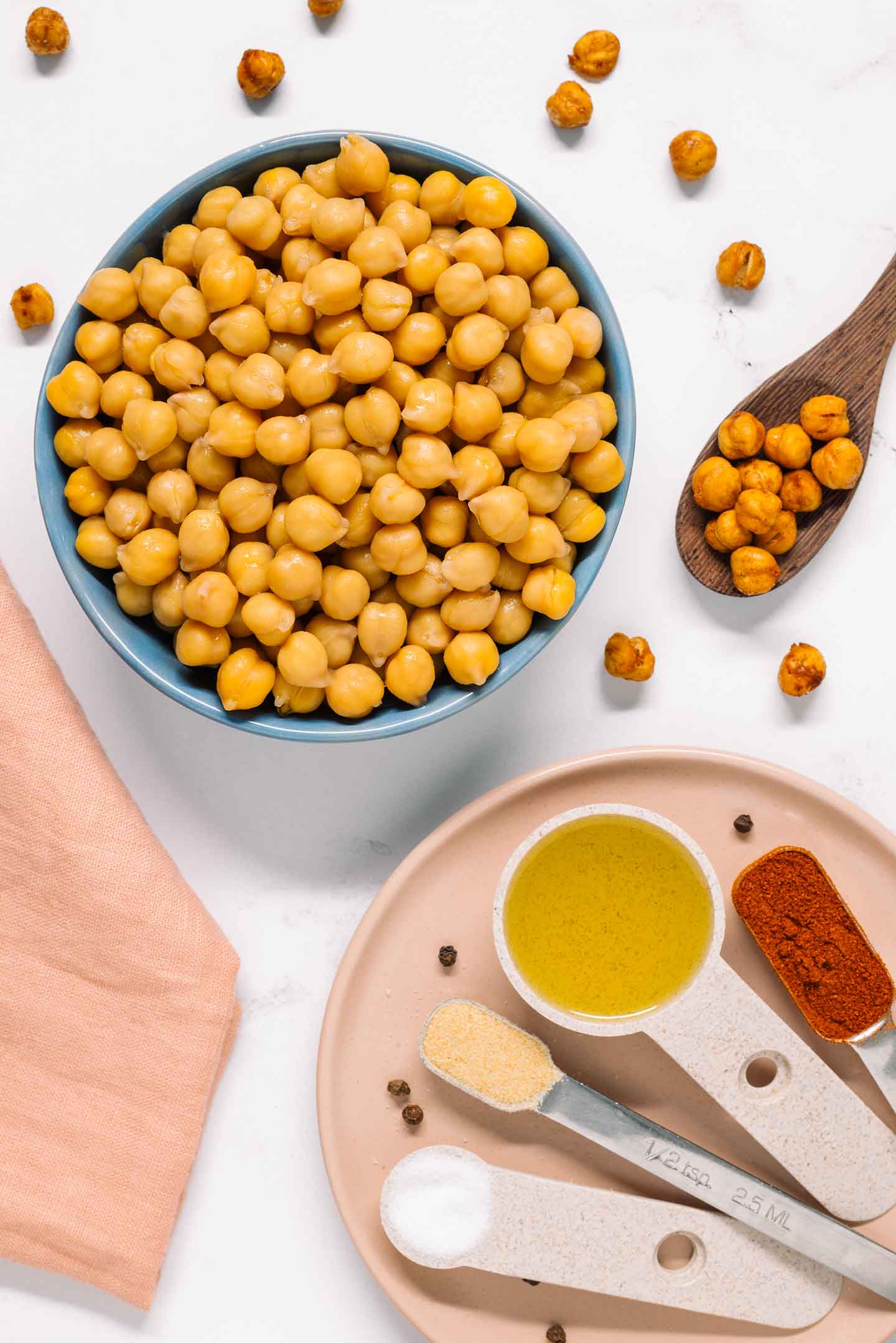 Top down view of ingredients for crunchy roasted chickpeas. The beans fill a small dish while seasonings are spread on a plate nearby.