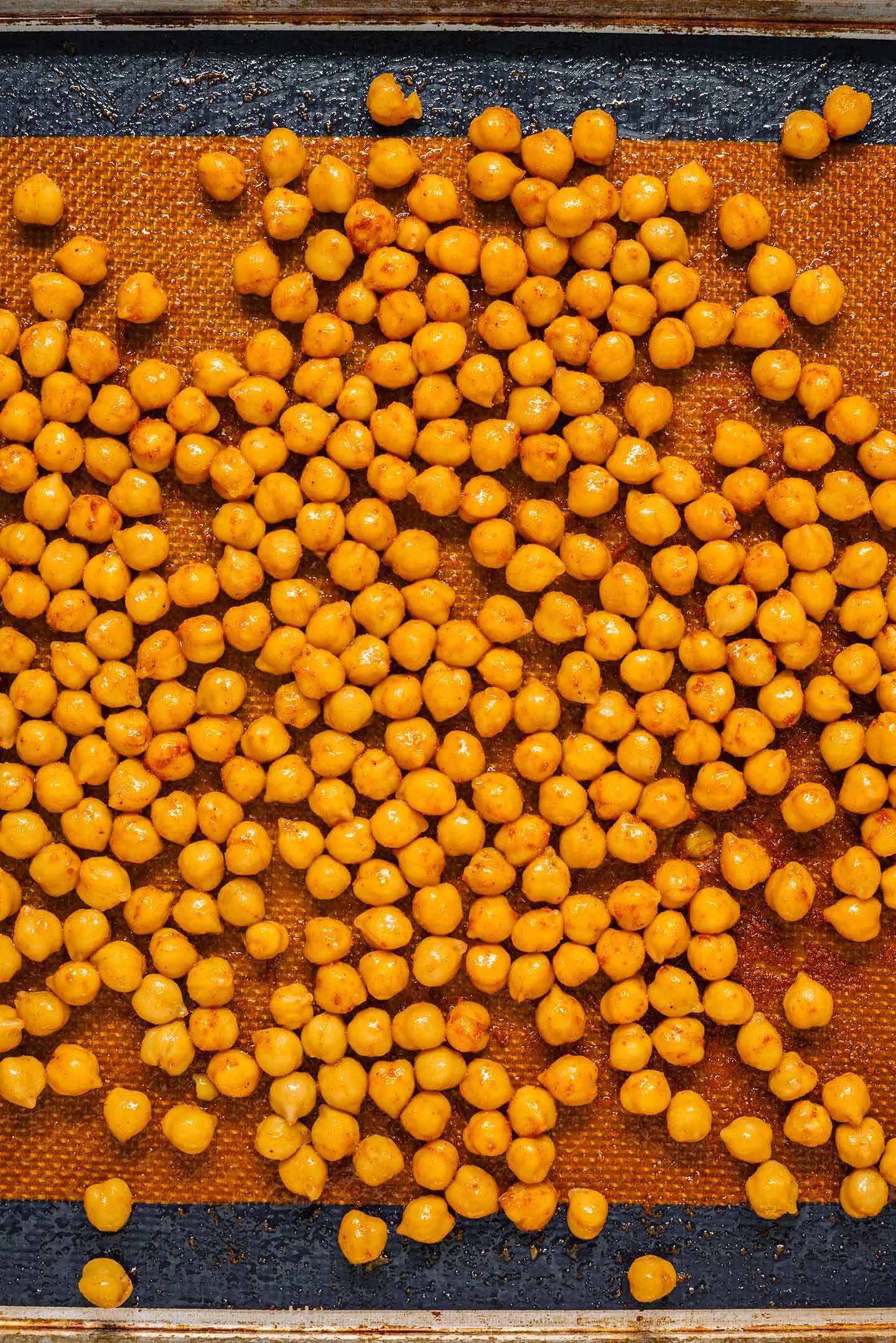 Top down view of chickpeas on a baking sheet coated with olive oil and seasonings.