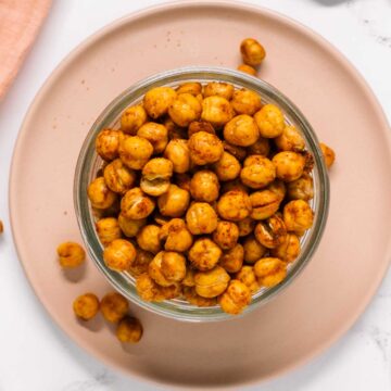 Top down view of crunchy roasted chickpeas in a small bowl. Chickpeas spill out onto a small plate beneath.