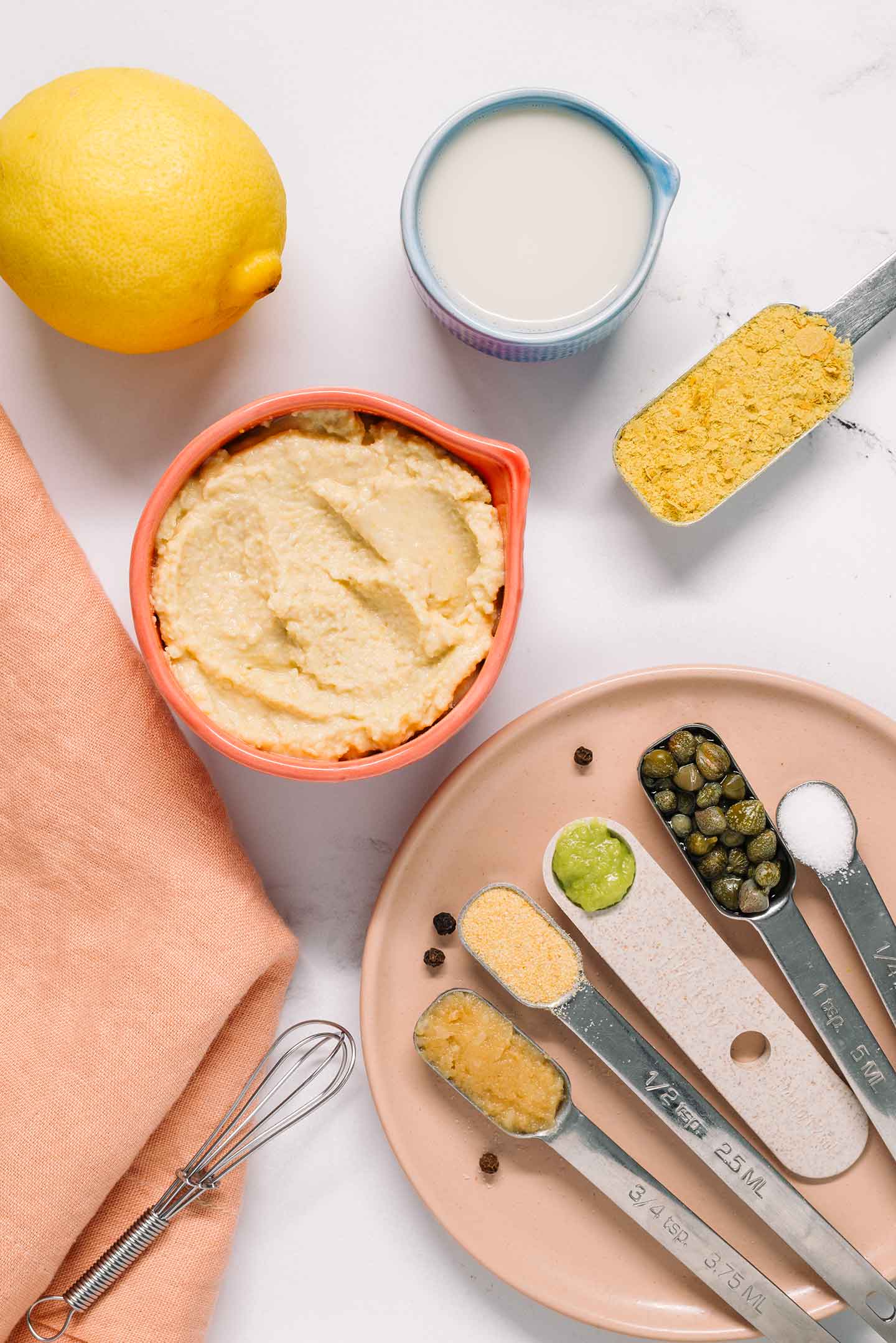 Top down view of ingredients. Hummus, lemon juice, nutritional yeast, and other seasonings fill the image.