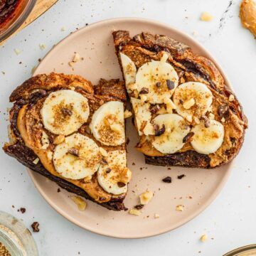 Top down view of an open-faced vegan Nutella sandwich topped with peanut butter, sliced banana, ground flax seed, cacao nibs, and toasted chopped walnuts.