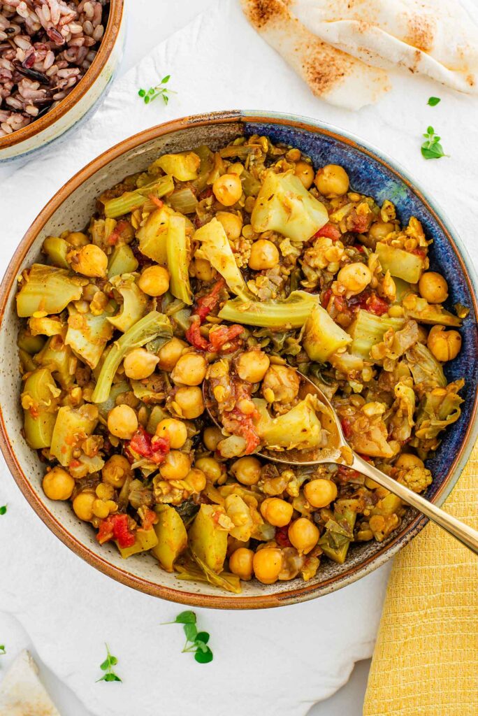 Top down view of a hearty bowl of cauliflower stem curry. The chunky curry is bulked up with red lentils, chickpeas, tomato and is full of aromatic spices.