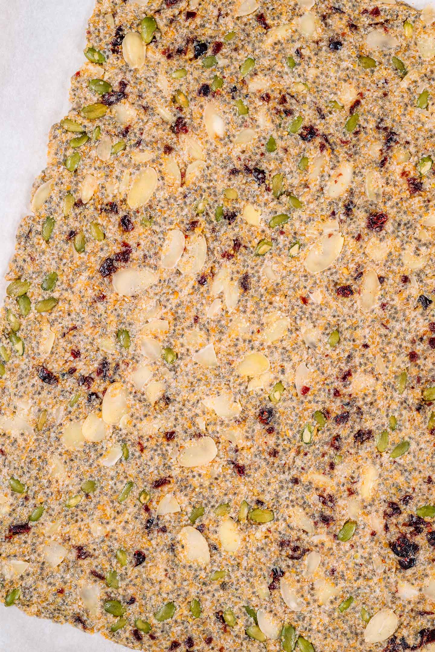Top down view of the holiday seed cracker mixture spread thinly on a baking sheet lined with parchment paper.
