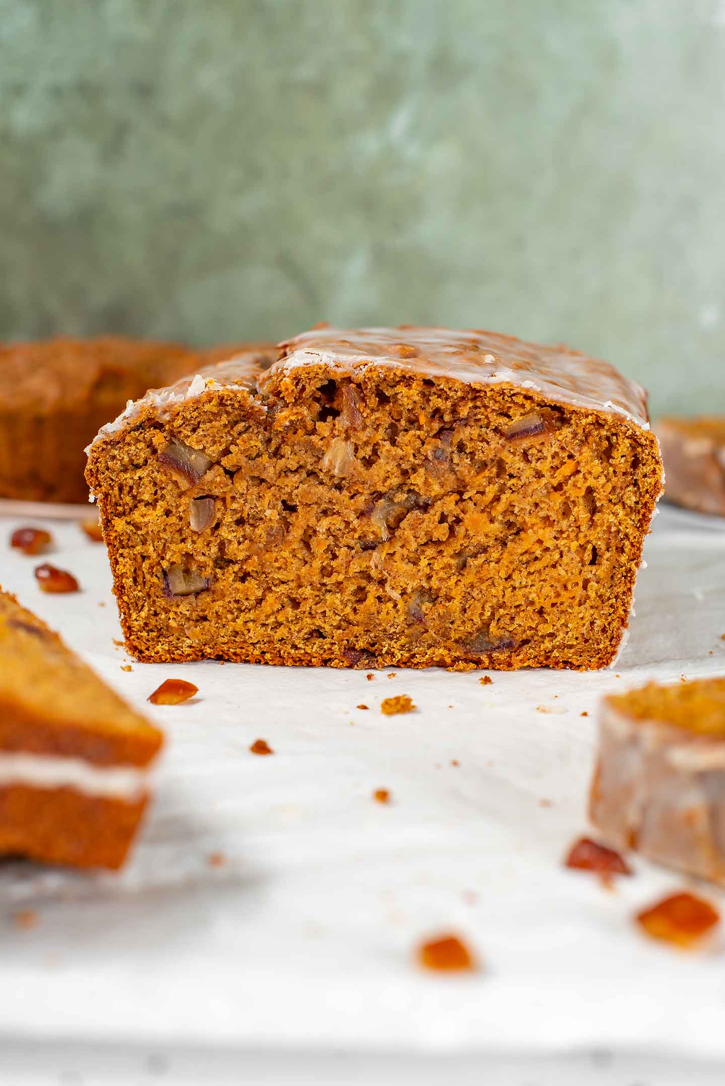 Close up of a sliced loaf of vegan sweet potato bread. The bread is golden in colour, speckled with dates, and thinly glazed.