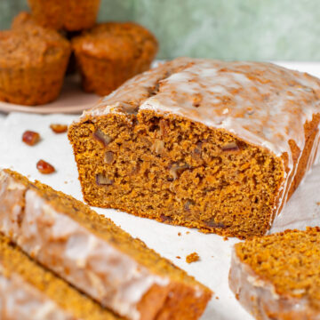 Side view of a glazed loaf of vegan sweet potato bread. The loaf has been cut exposing the tender crumb speckled with chopped dates.