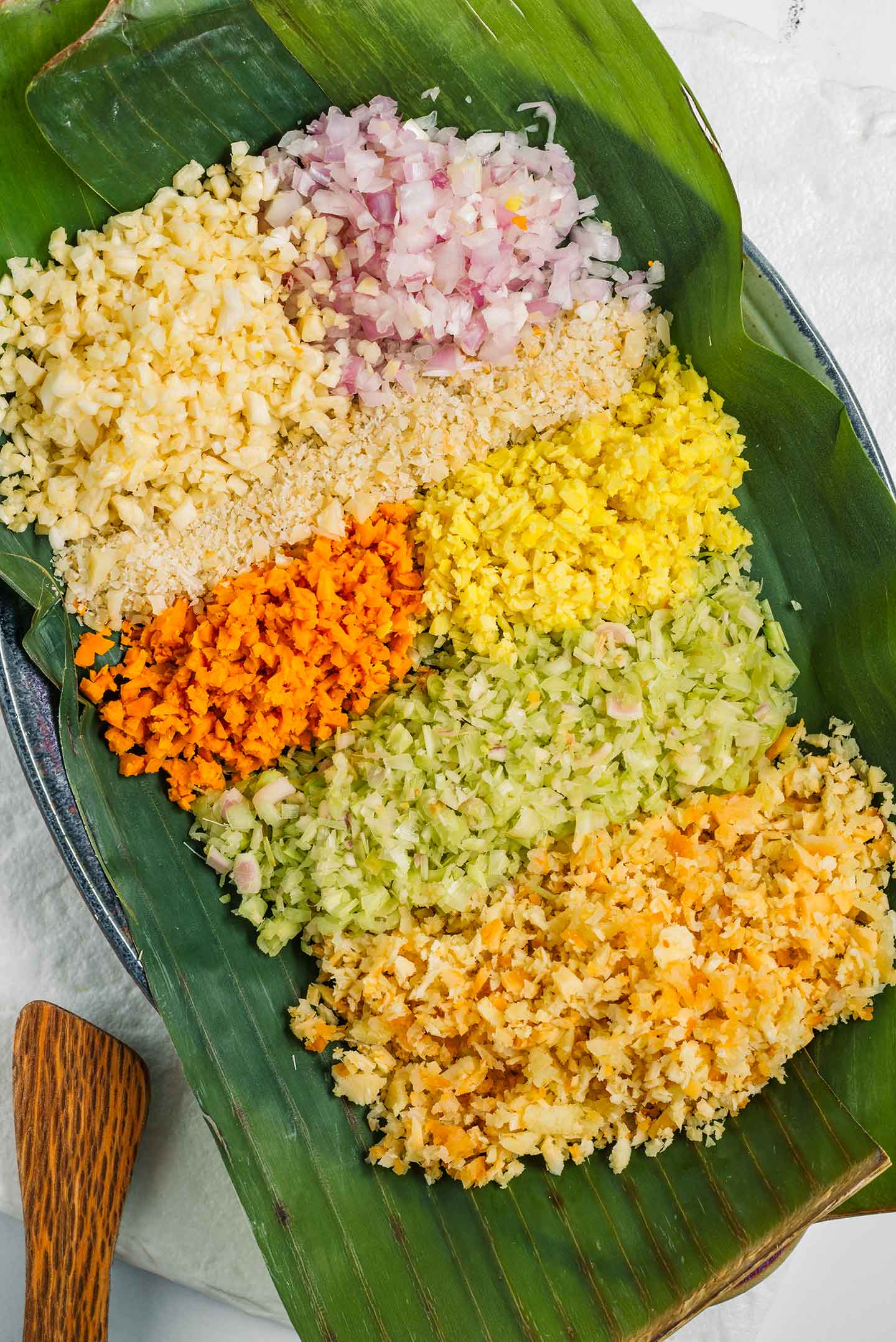 Top down view of the ingredients for basa bali spice paste minced and portioned on a banana leaf.