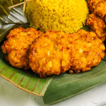 Close-up of three Indonesian perkedels on a platter lined with banana leaves. The vegan Indonesian corn fritters are golden and crispy.