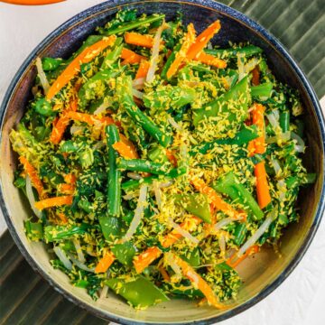 A Balinese coconut vegetable salad called "urab" fills a shallow bowl. The salad is a mixture of leafy greens, green beans, snow peas, bean sprouts and carrots coated in spiced toasted coconut.