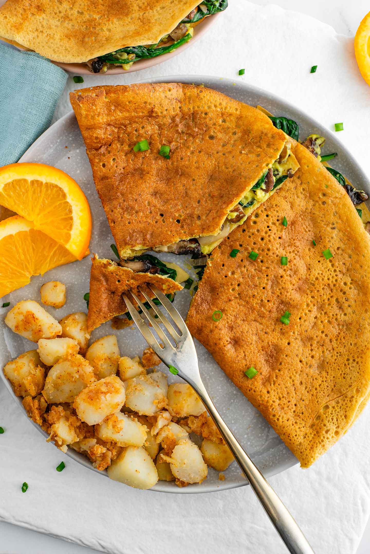 Top down view of a golden vegan omelette. The chickpea omelette is sliced to reveal a filling of mushrooms, spinach, onion, and homemade vegan cheese. 