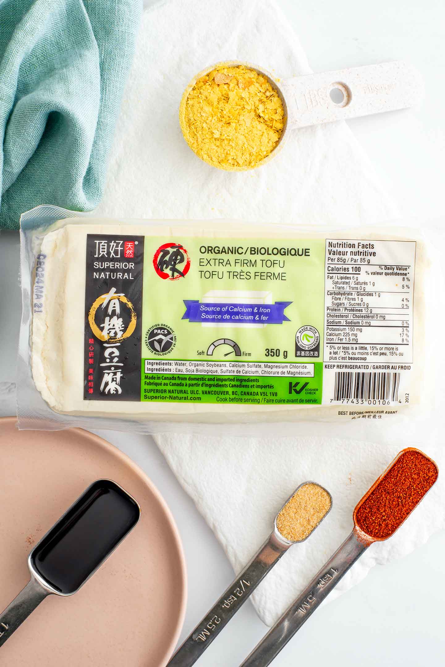 Top down view of ingredients. A storebought package of pressed extra firm tofu is surrounded by nutriitonal yeast, tamari, garlic powder, and smoked paprika. 