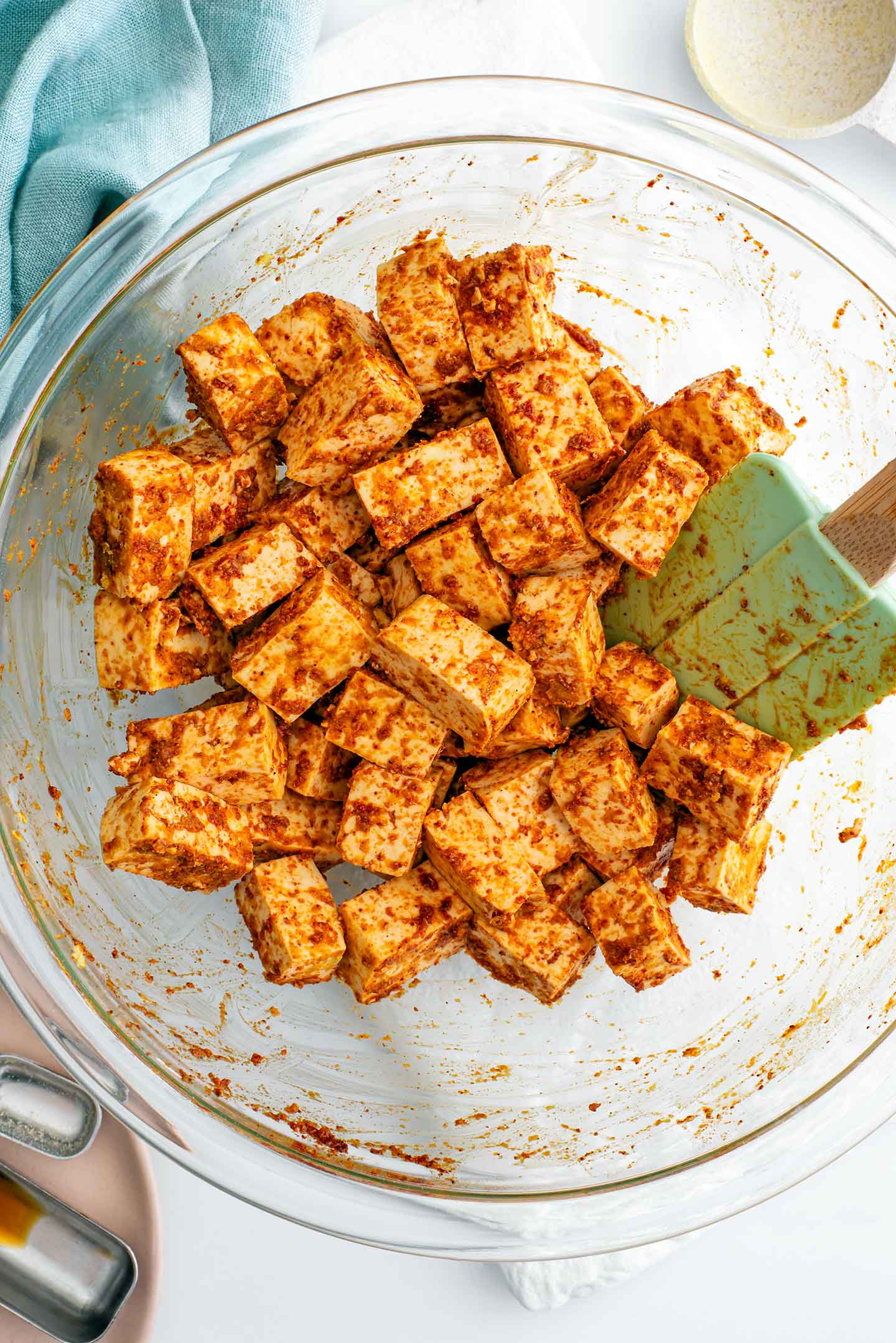 Top down view of tofu cubes being tossed in seasonings in a large glass bowl.