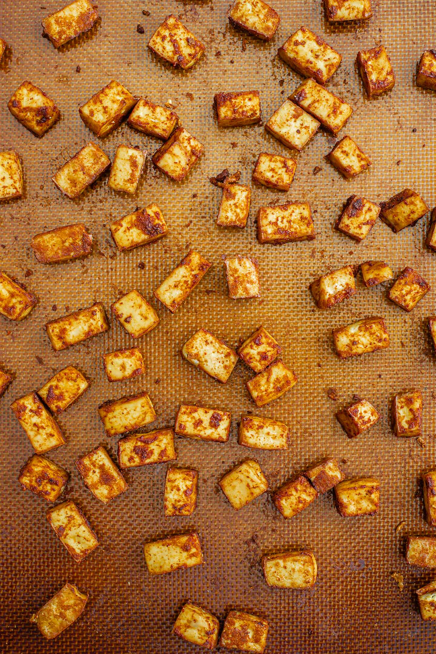 Top down view of crispy baked tofu fresh from the oven and spread on a baking sheet lined with a silicone mat.