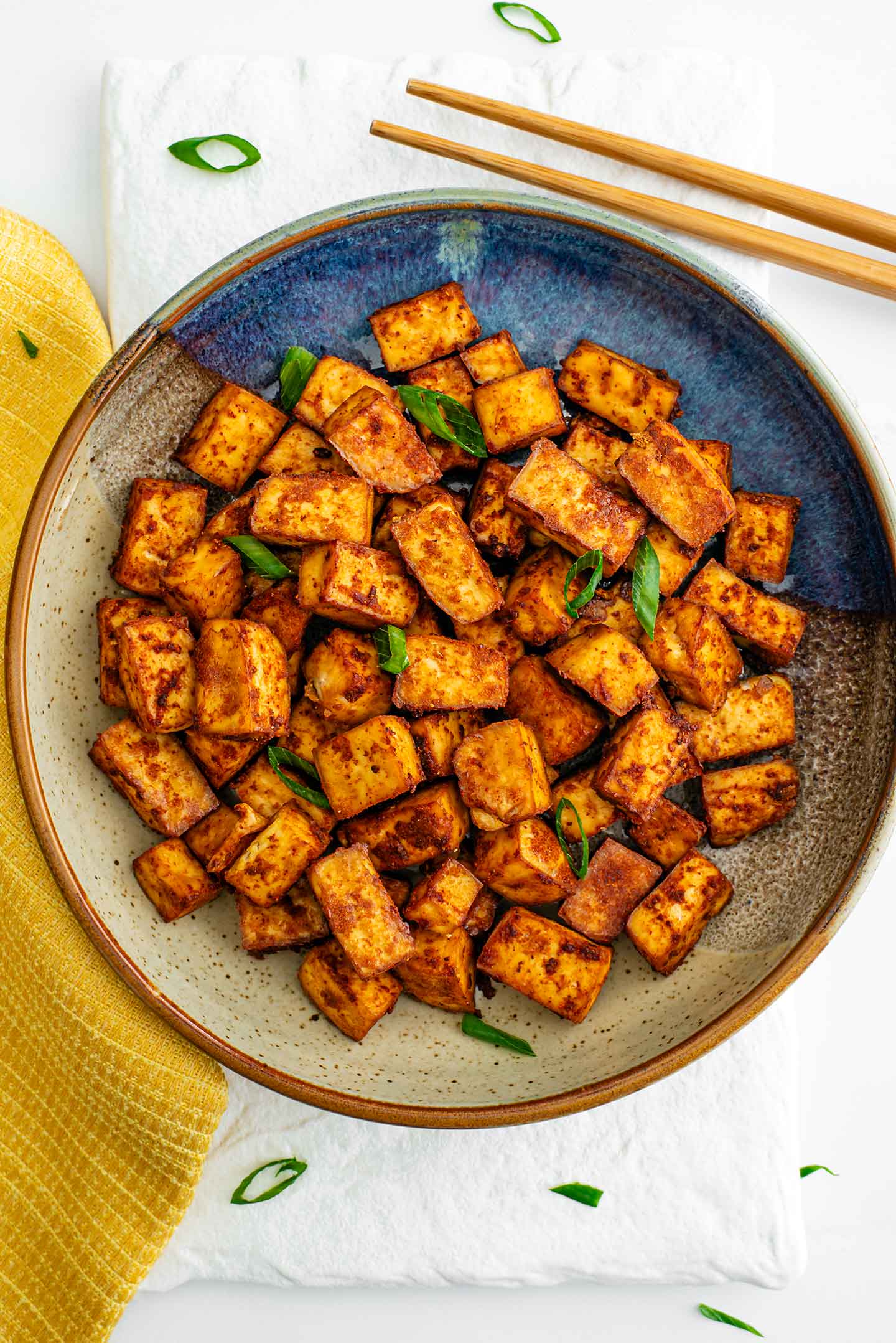 Top down view of crispy baked tofu cubes in a bowl garnished with green onion. The tofu is dark golden brown and crispy on the edges.