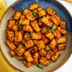 Top down view of crispy baked tofu cubes in a bowl garnished with green onion.