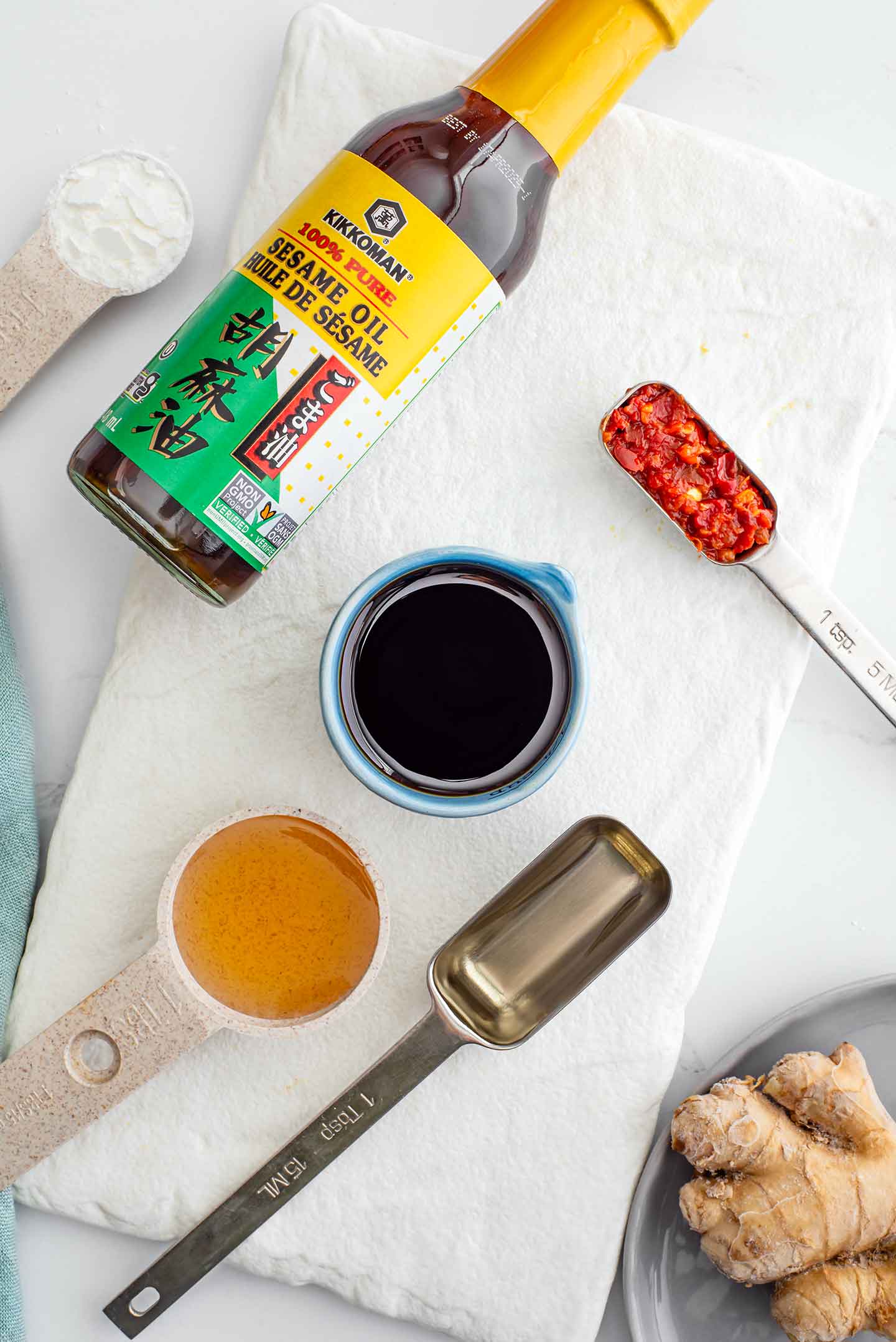 Top down view of ingredients for stir fry sauce. Sesame oil, tamari, rice vinegar, maple syrup, chili garlic sauce, ginger root, and cornstarch.