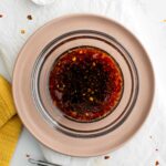 Top down view of a dark stir fry sauce in a small glass bowl. The sauce is speckled with garlic, ginger and chili flakes.