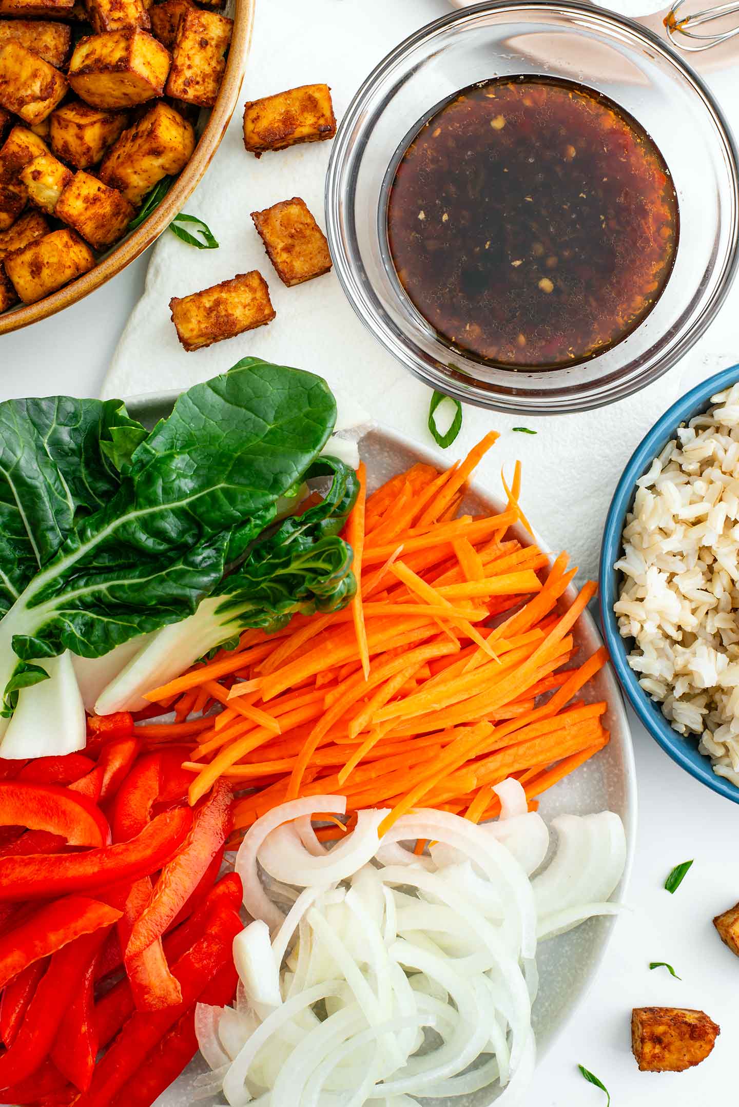 Top down view of all the components of my stir fry recipe. Rice, crispy tofu, sliced vegetables and homemade stir fry sauce.