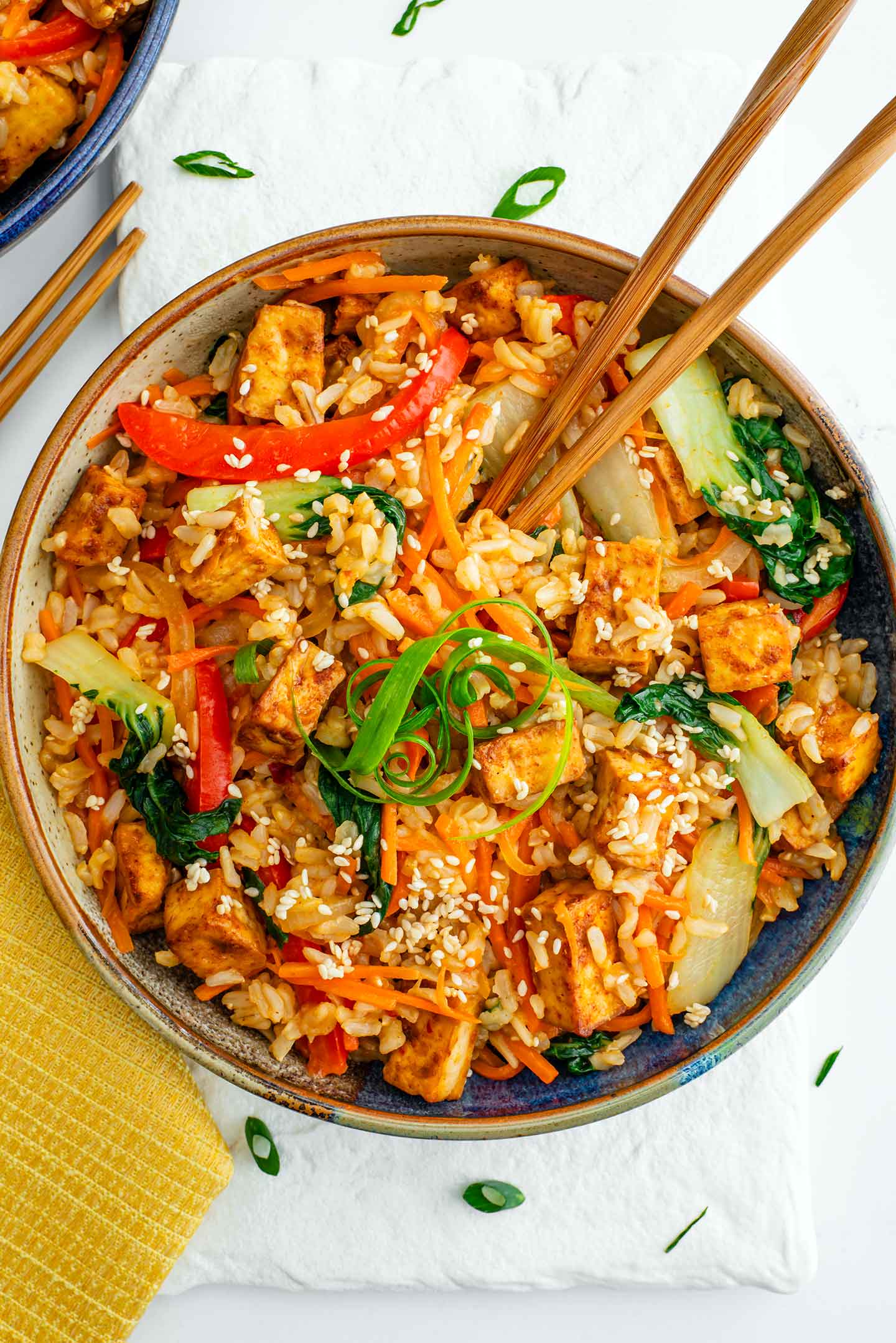 Top down view of a bowl of stir fry with crispy tofu. Chopsticks rest in the stir fried rice and vegetables.