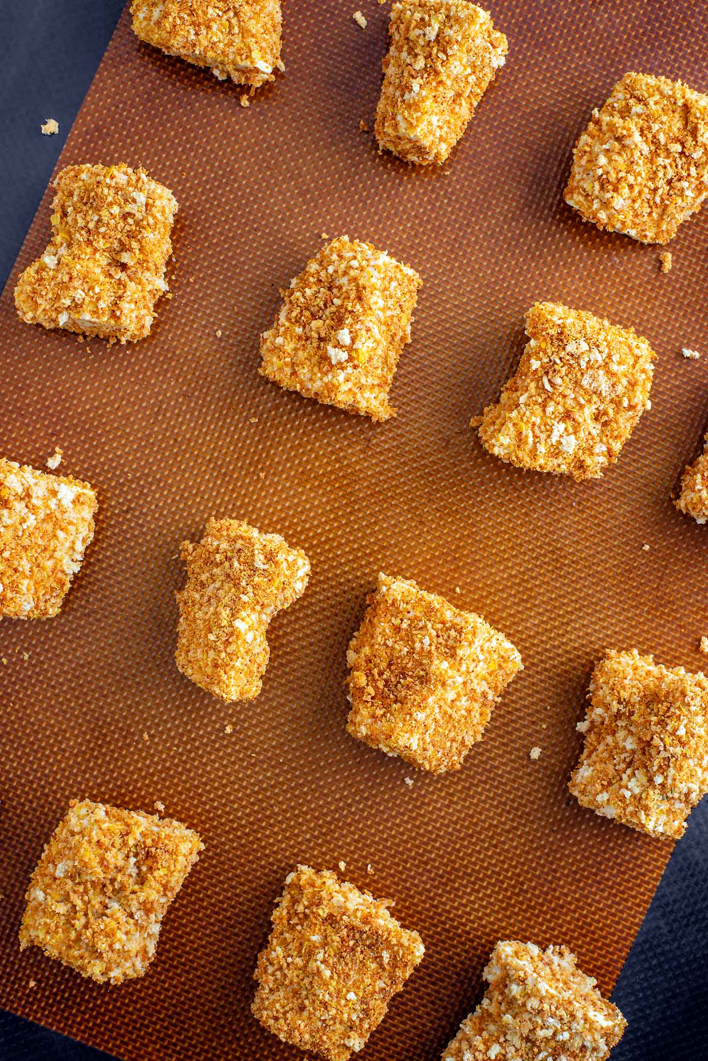 Top down view of golden and crispy tofu nuggets on a baking tray lined with a silicone mat.