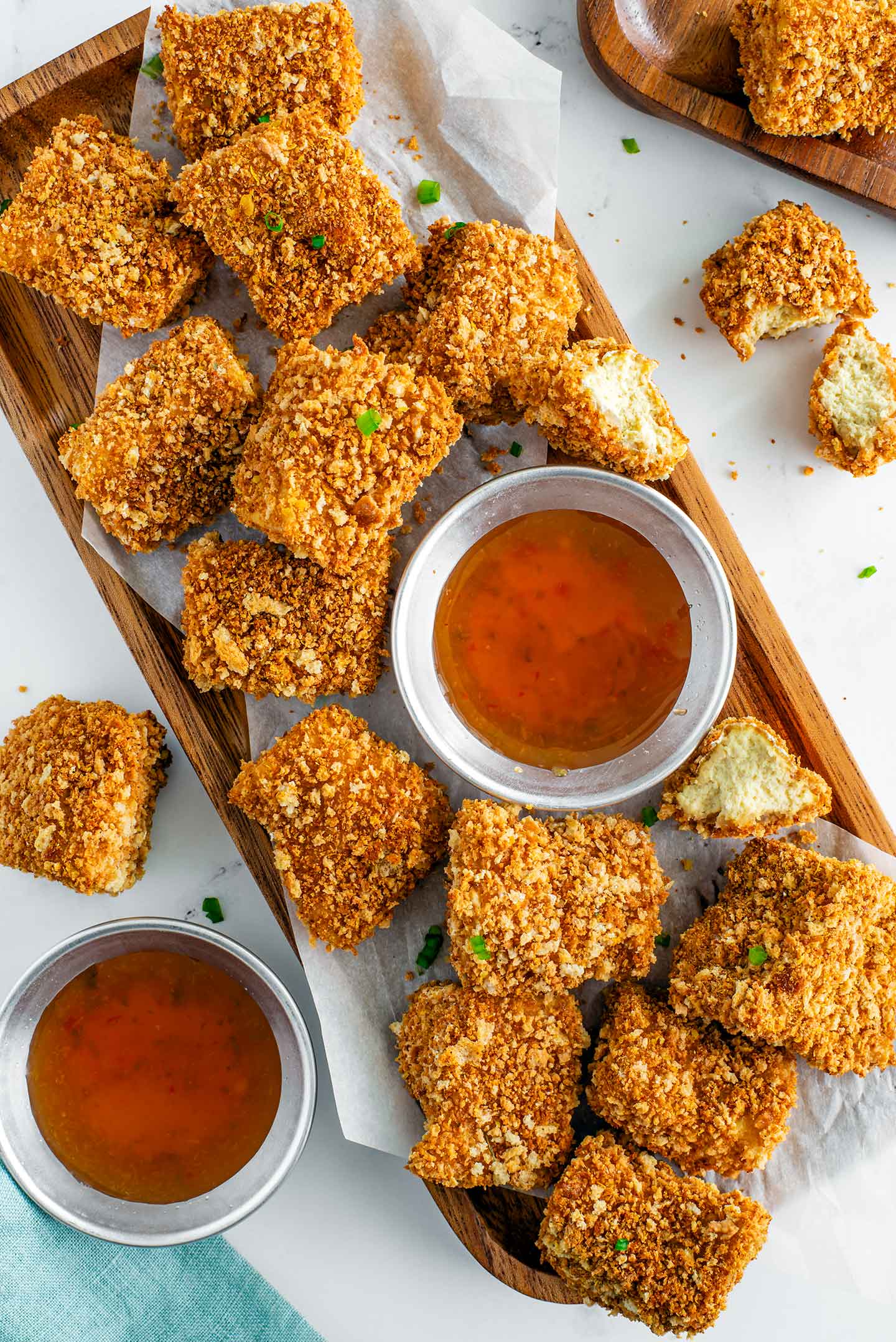 Top down view of a tray littered with crispy and golden baked tofu nuggets. Small bowls of dipping sauce are ready for dunking.