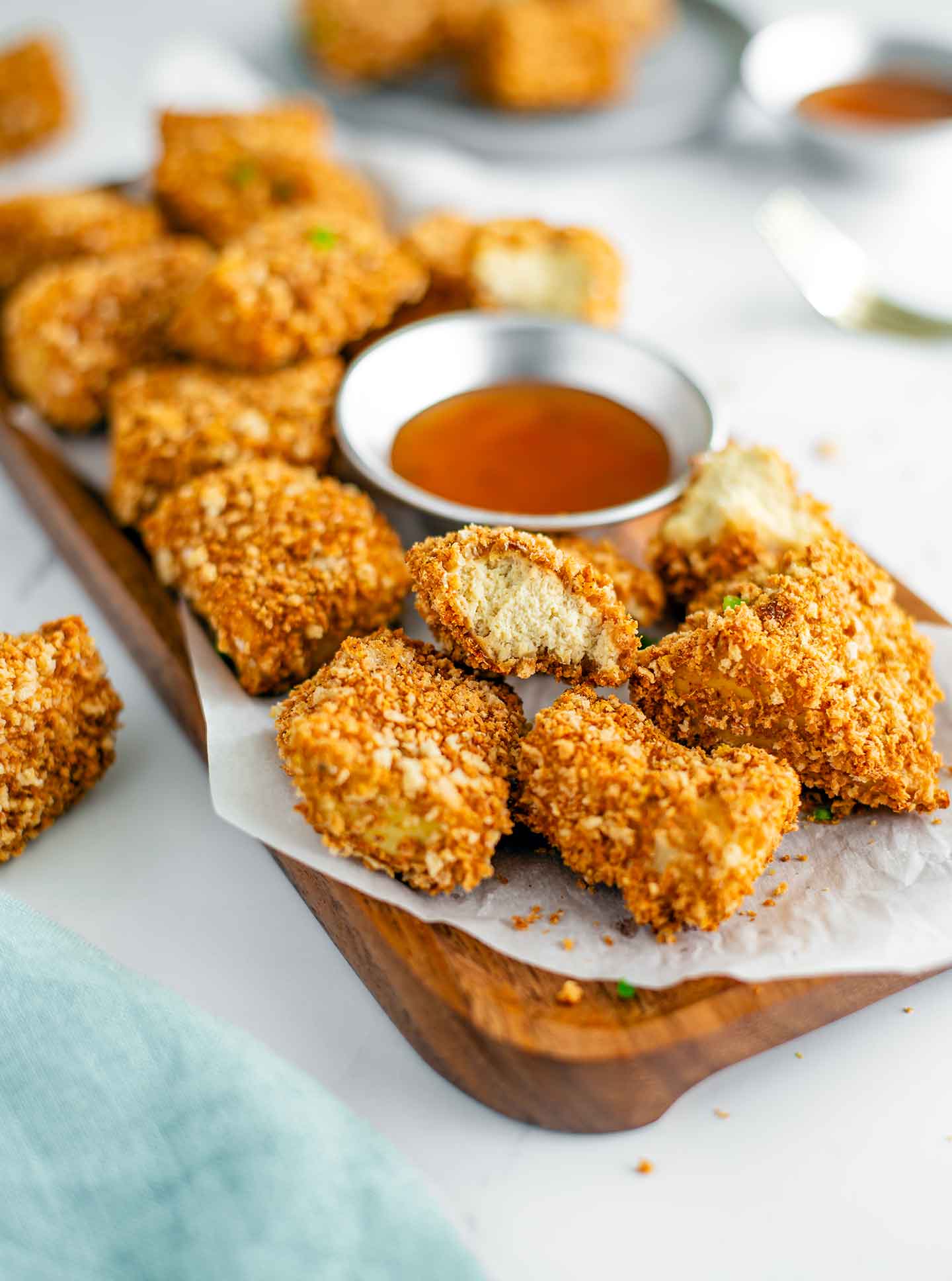 Close up of baked tofu nuggets on a tray with a dipping sauce. The white tofu centre of one golden nugget is displayed. The rest are crispy and golden.