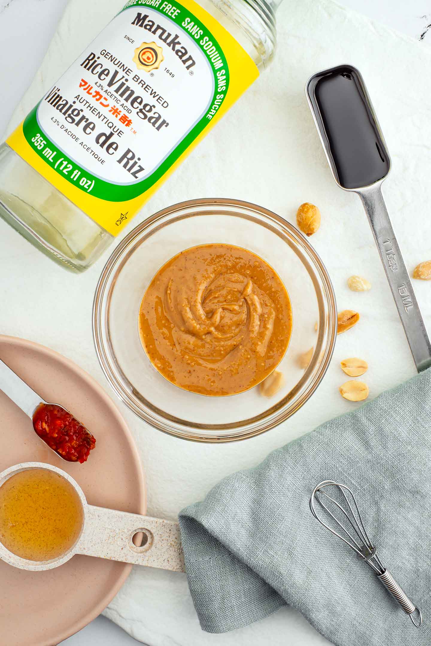 Top down view of ingredients for a peanut dressing. Peanut butter, rice vinegar, tamari, maple syrup, and chilli garlic sauce.