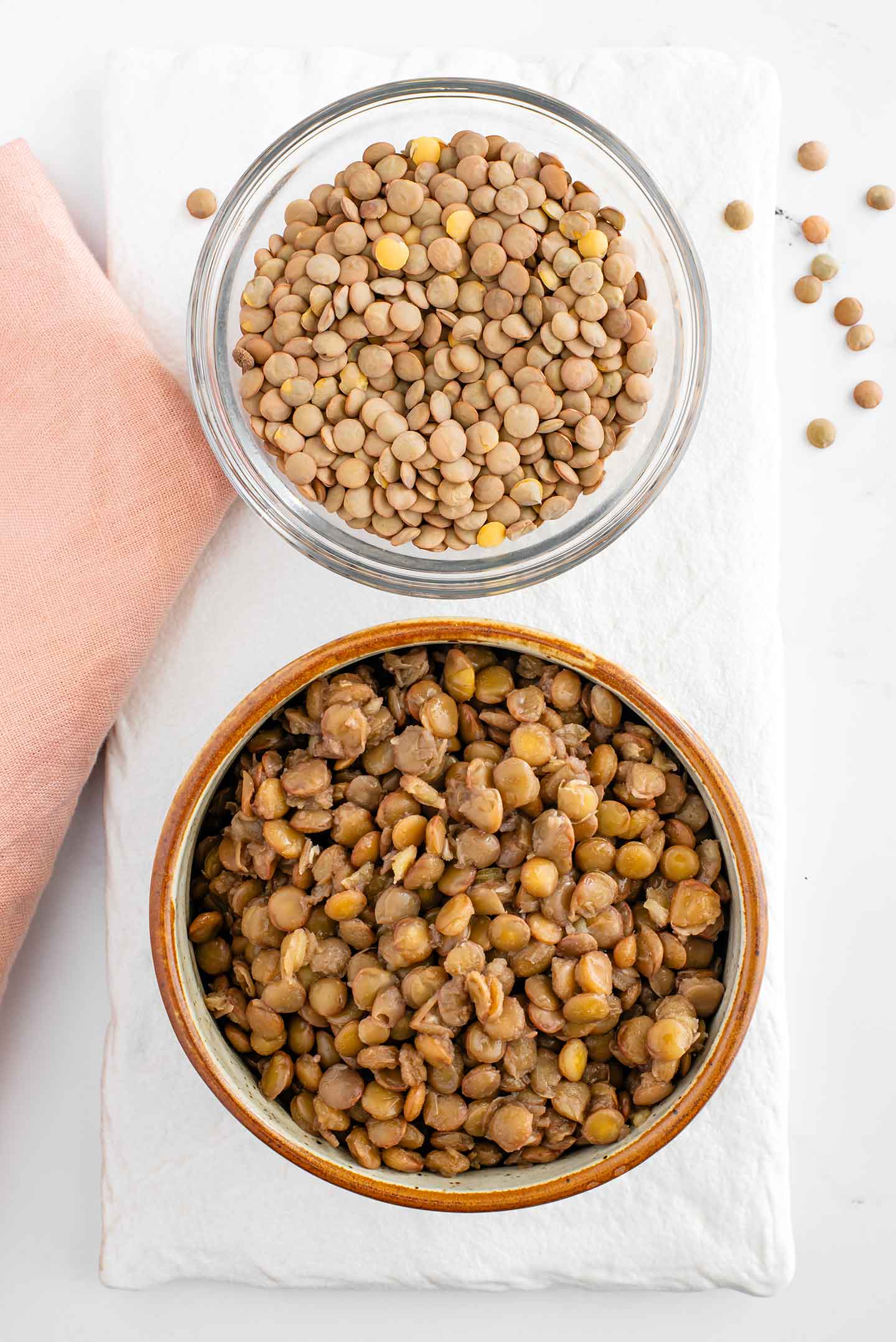 Top down view of a bowl containing raw green lentils next to a bowl of cooked green lentils. 