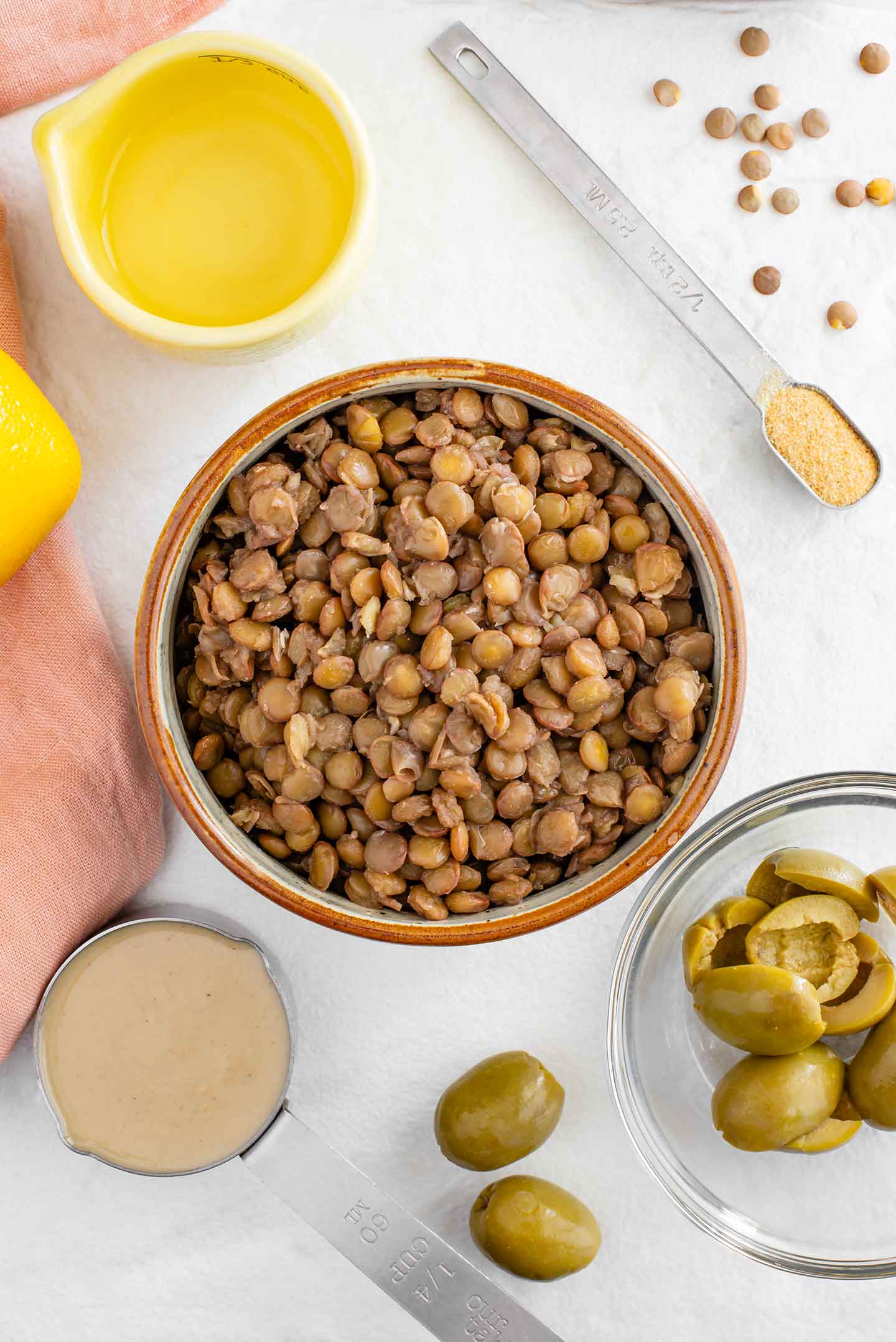 Top down view of ingredients on a white tray. Cooked green lentils, tahini, green olives, lemon juice, and garlic powder.