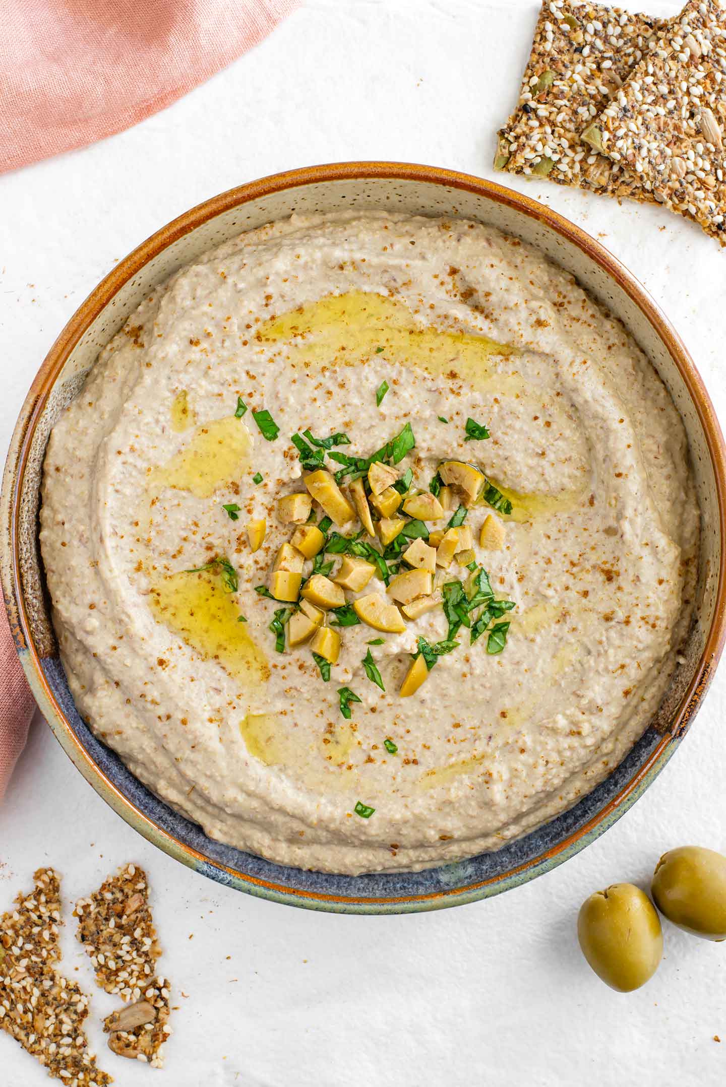 Top down view of creamy green lentil hummus in a shallow bowl garnished with chopped green olives, minced basil, and a drizzle of olive oil.