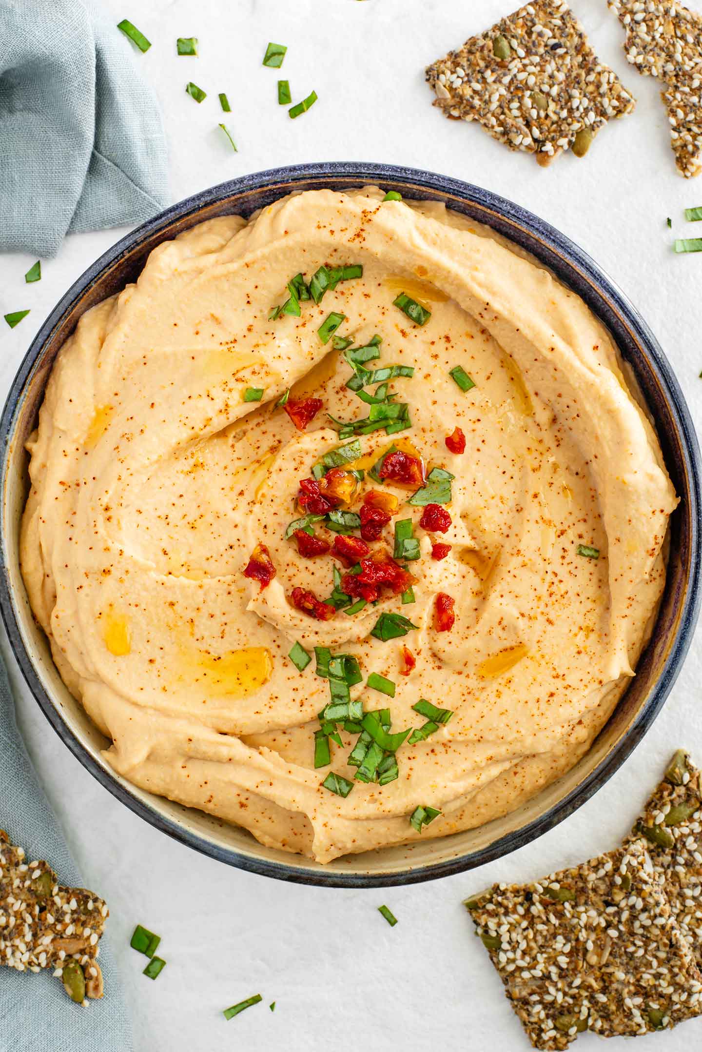 Top down view of creamy red lentil hummus in a shallow dish. The light pink coloured hummus is garnished with chopped sun-dried tomatoes and minced basil.