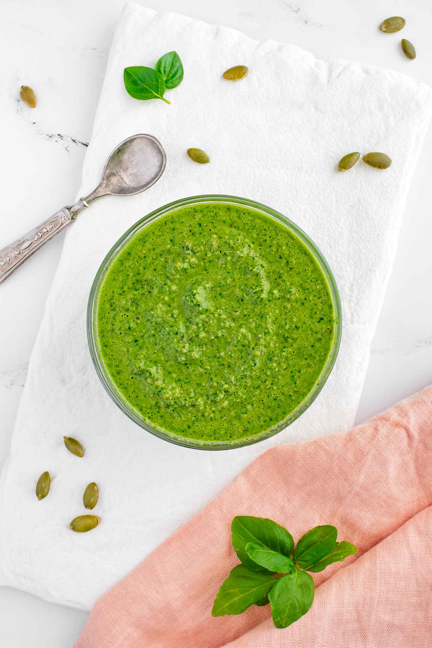 Top down view of a small bowl of vegan pesto sauce. The blended sauce is bright green with flecks of texture from the basil leaves and pumpkin seeds. 