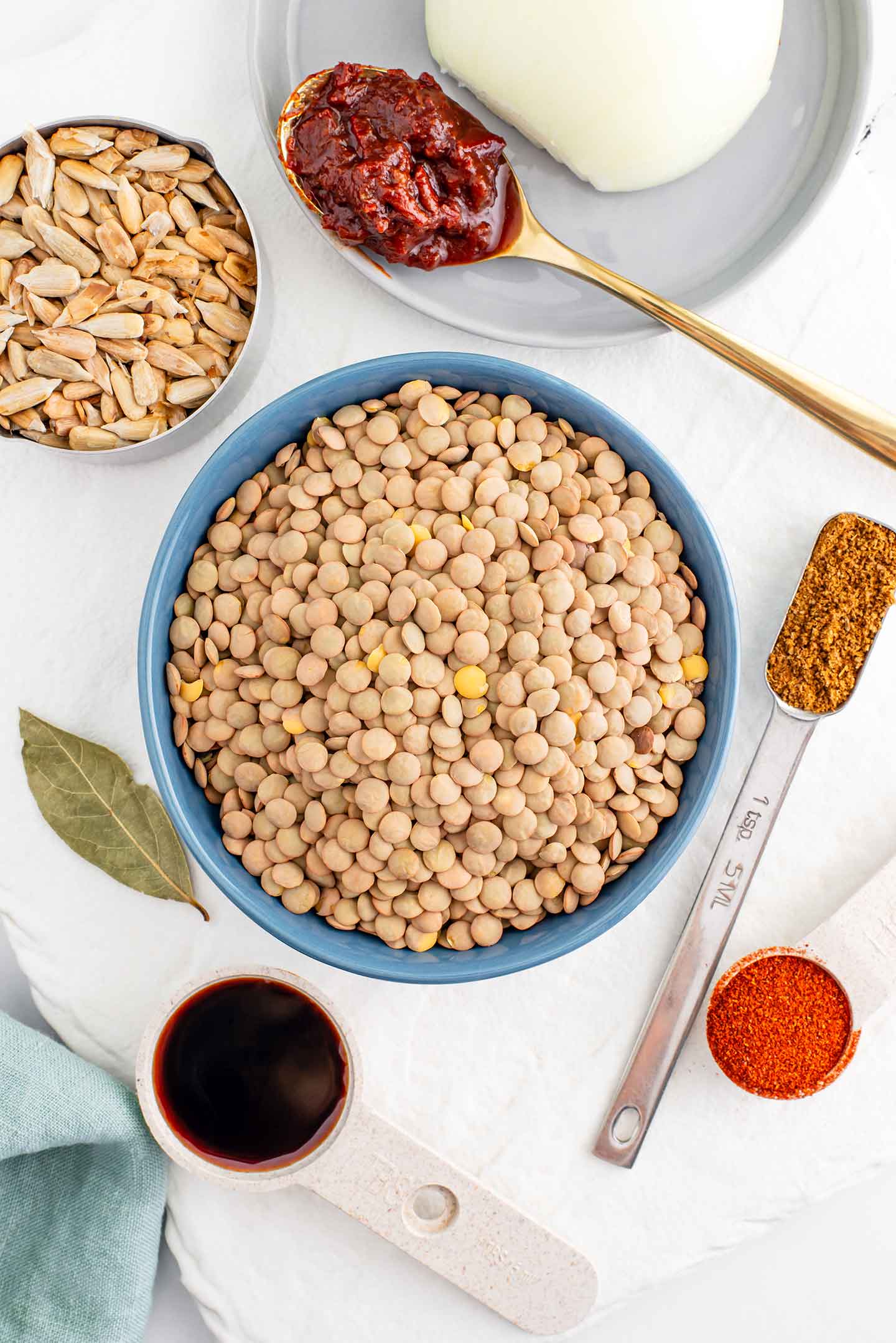 Top down view of ingredients for lentil meat. Dry green lentils, toasted sunflower seeds and seasonings are displayed on a white tray.