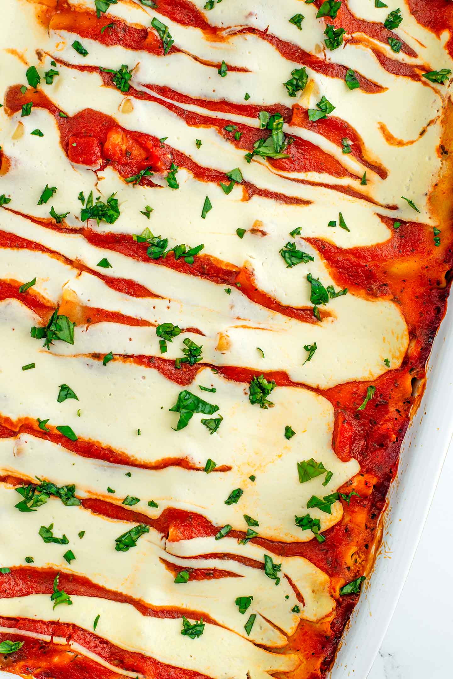 Top down view of a baked lasagna with crispy edges, a lightly golden tofu cheese sauce, and chopped basil. 