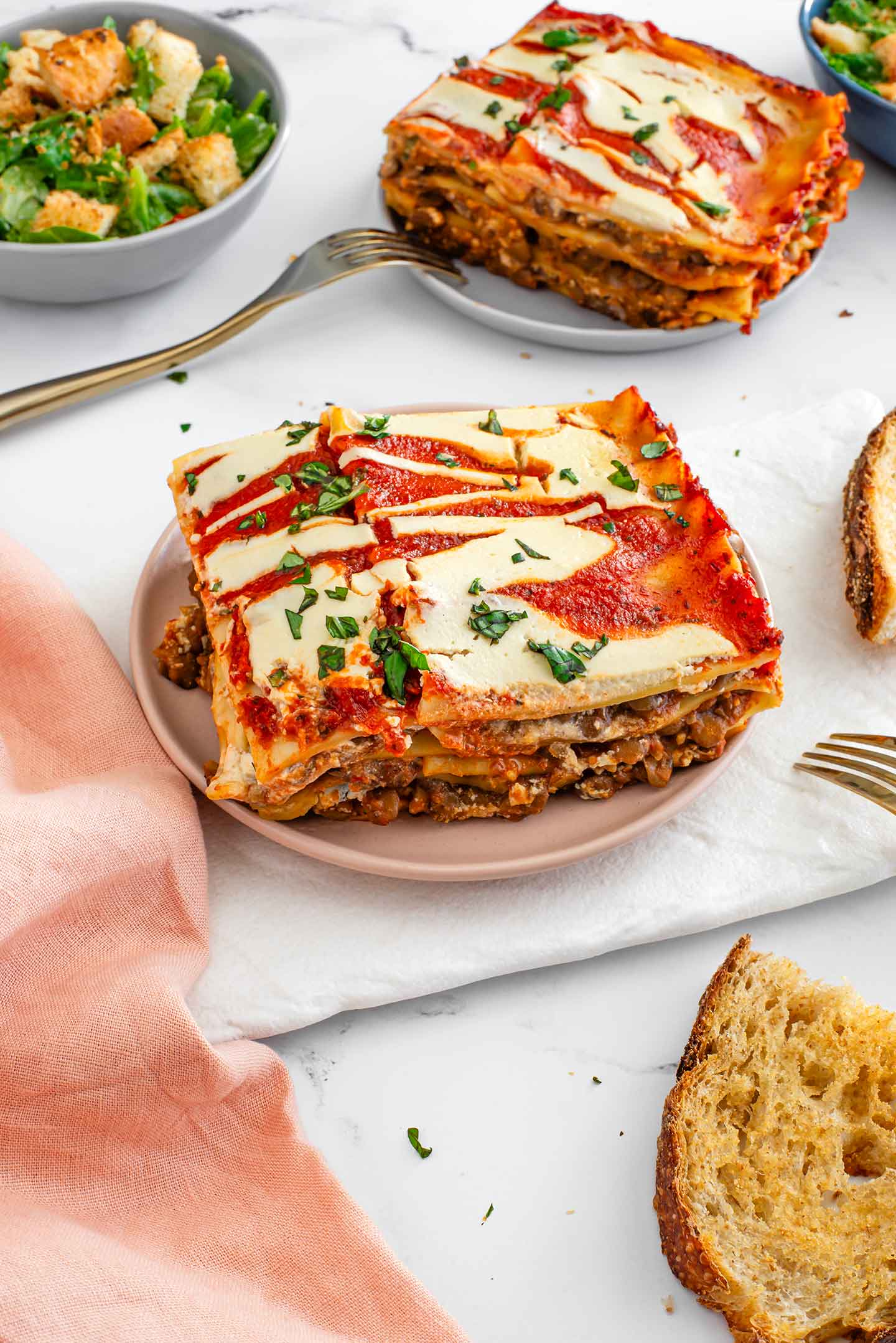 Top down view of two slices of lentil lasagna with garlic bread and caesar salad. 