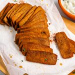 Slices of golden and juicy tofu shaved meat are laid out on a piece of parchment paper. The tofu meat looks textured and spiced.