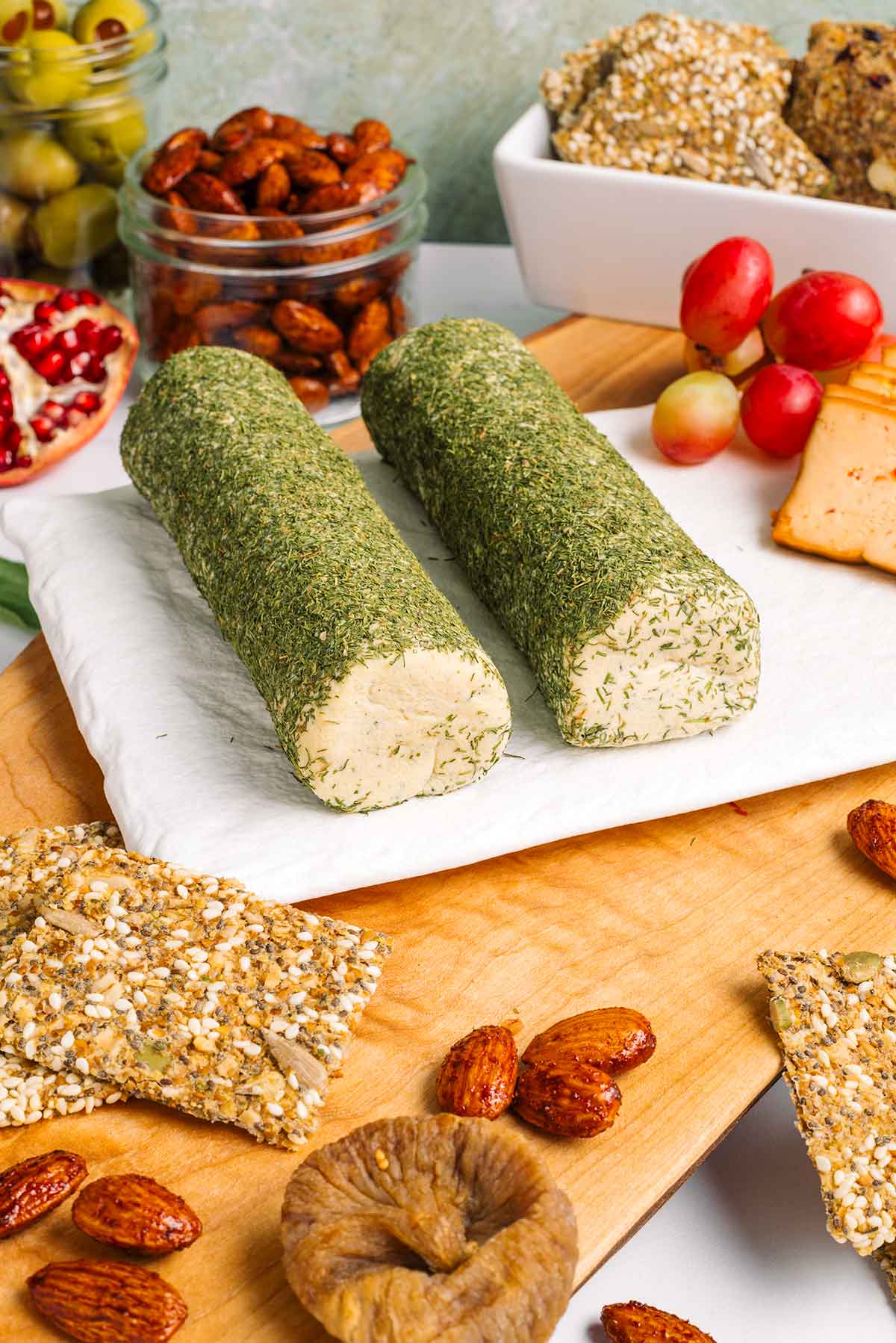 Side view of a garlic and dill vegan cheese log split in two. The cheese is garnished with dill and the centrepiece of a vegan charcuterie board.