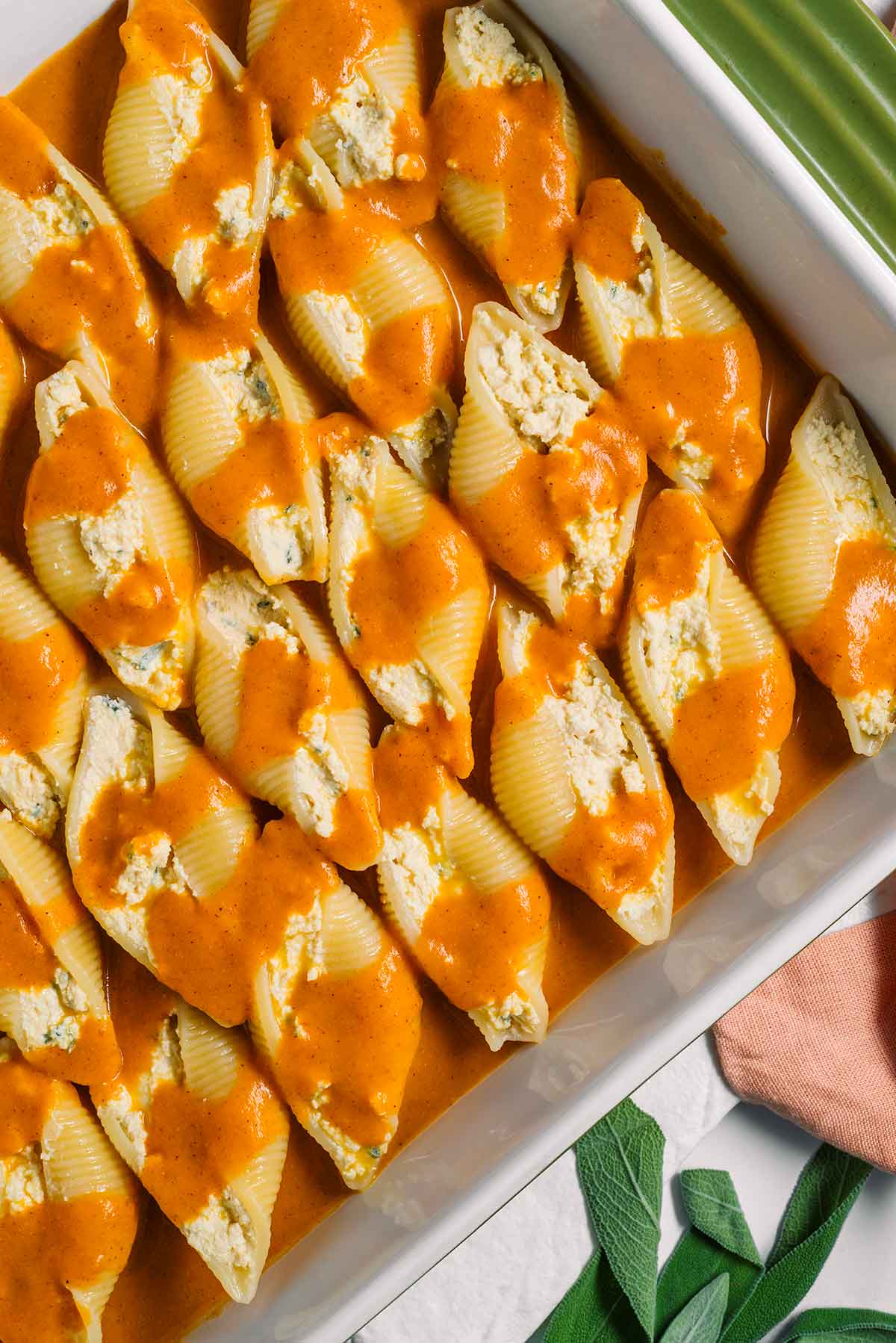 Top down view of vegan stuffed shells in a casserole dish before being baked. The shells are stuffed with ricotta and a pumpkin sauce is delicately drizzled overtop.