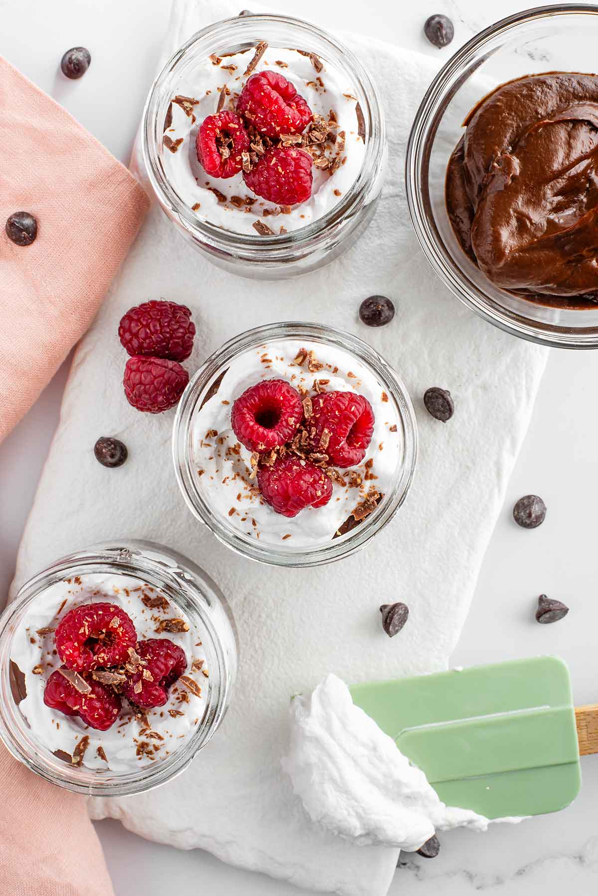 Top down view of chocolate avocado pudding cups topped with coconut whipped cream and three fresh raspberries.