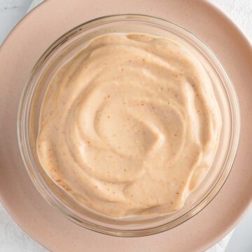 Top down view of thick and creamy vegan Russian dressing in a small bowl. The dressing has a light pink hue and is speckled with seasonings.