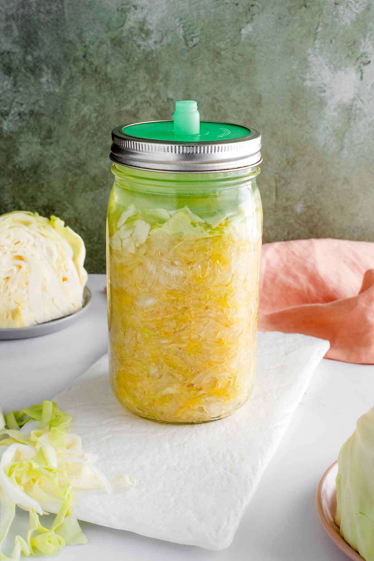 Side view of a jar of homemade sauerkraut partway through the fermentation process. The shredded cabbage fills a glass jar and is held down with a fermentation weight. A pickle pipe fermentation lid is secured on the top of the jar.