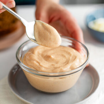 Side view of a hand lifting a spoon of creamy vegan Russian dressing from a bowl of the pink tinged dressing.