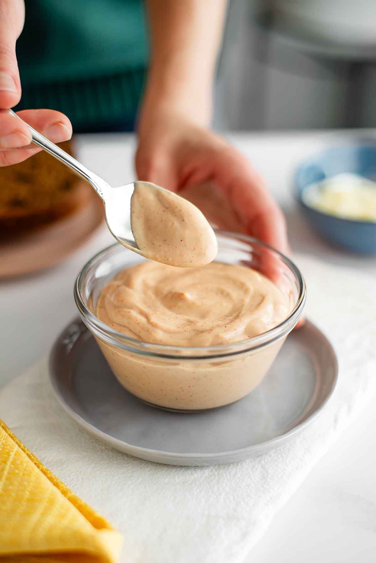 Side view of a hand lifting a spoon of creamy vegan Russian dressing from a bowl of the pink tinged dressing. The dressing is thick and luscious with small speckles of spice throughout.