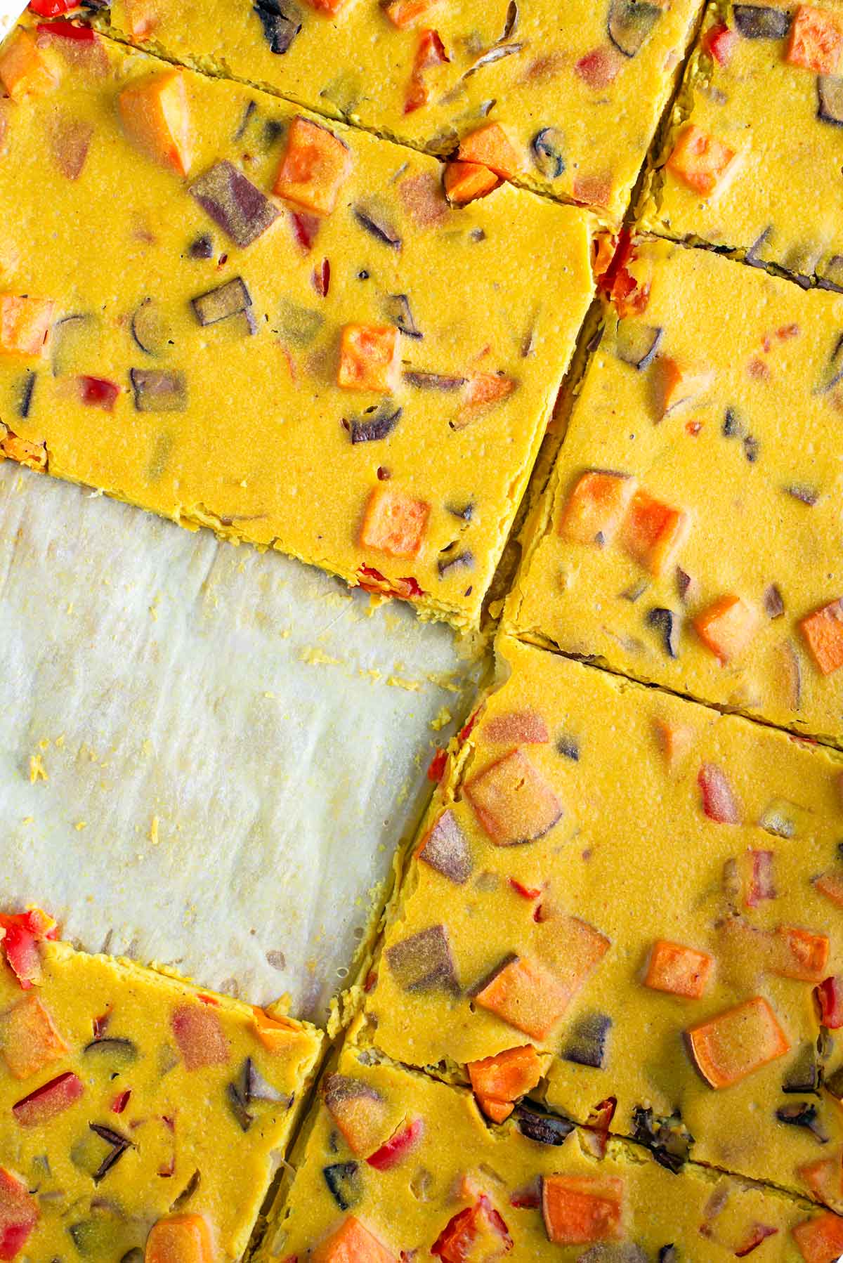 Top down view of a cooked vegan "egg" and vegetable patty sliced into eight equal portions. One portion has been removed from the pan.