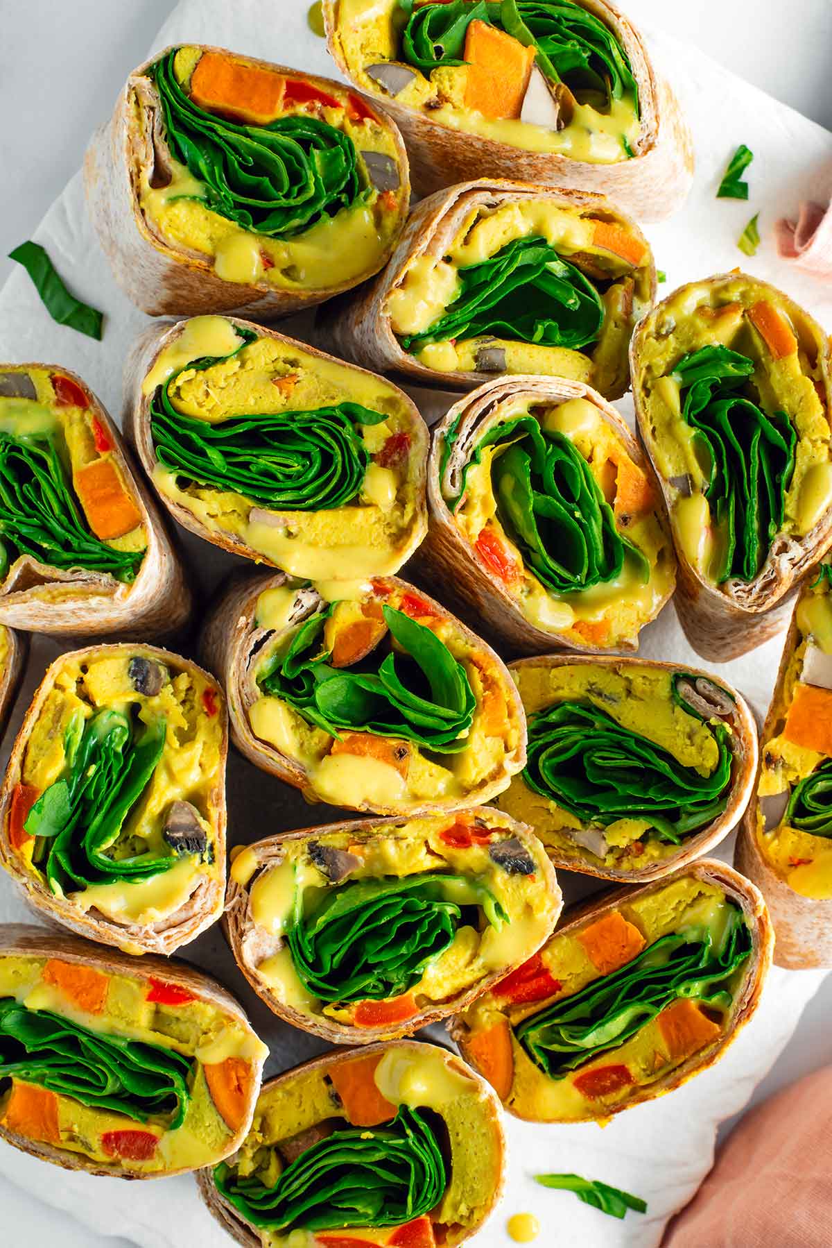 Top down view of a tray full of meal prepped vegan breakfast burritos. They are all filled with a vegan egg and vegetable patty, fresh spinach, and vegan queso.