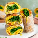 Side view of stacked vegan breakfast burritos. They are filled with a vegan egg and vegetable patty, fresh spinach, and a runny vegan queso.