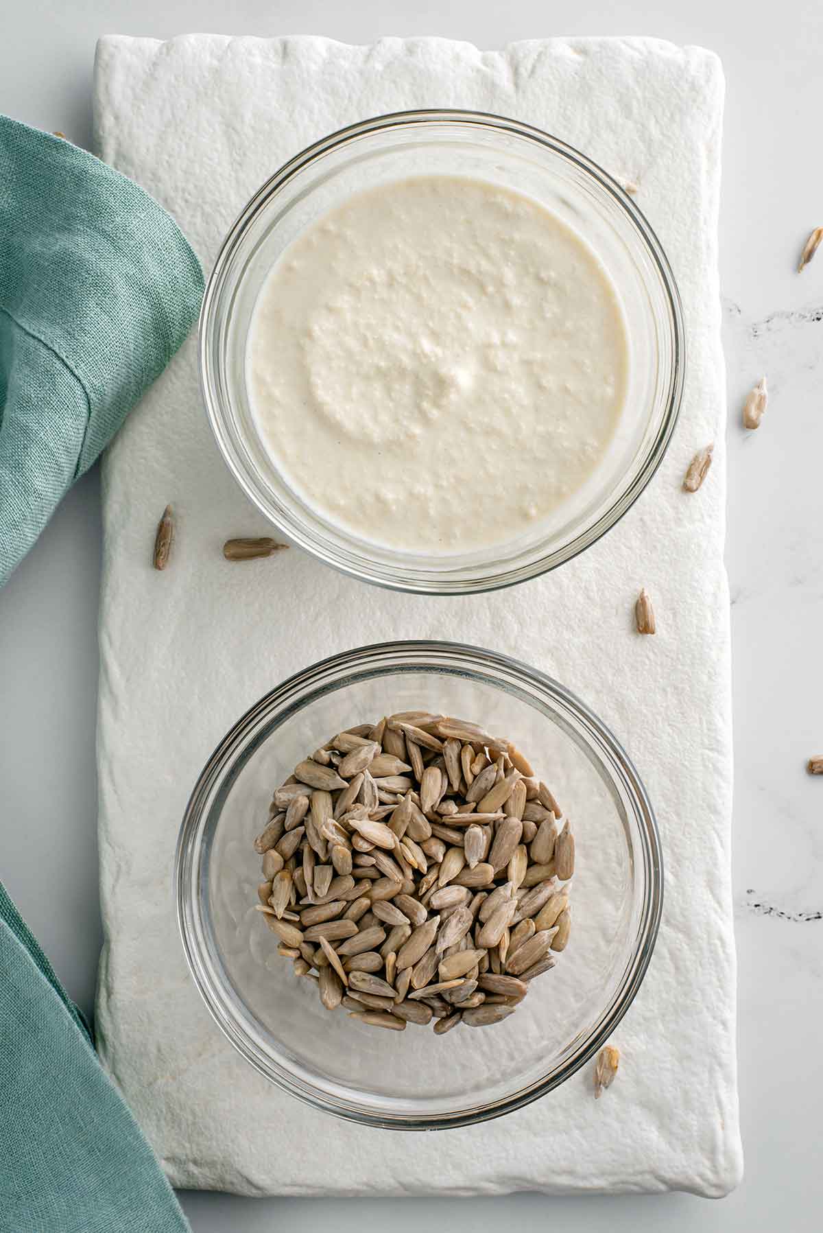 Top down view of two small bowls on a white tray. One bowl is filled with sunflower seeds. The other bowl is filled with a creamy but slightly textured sunflower seed "mayonnaise".