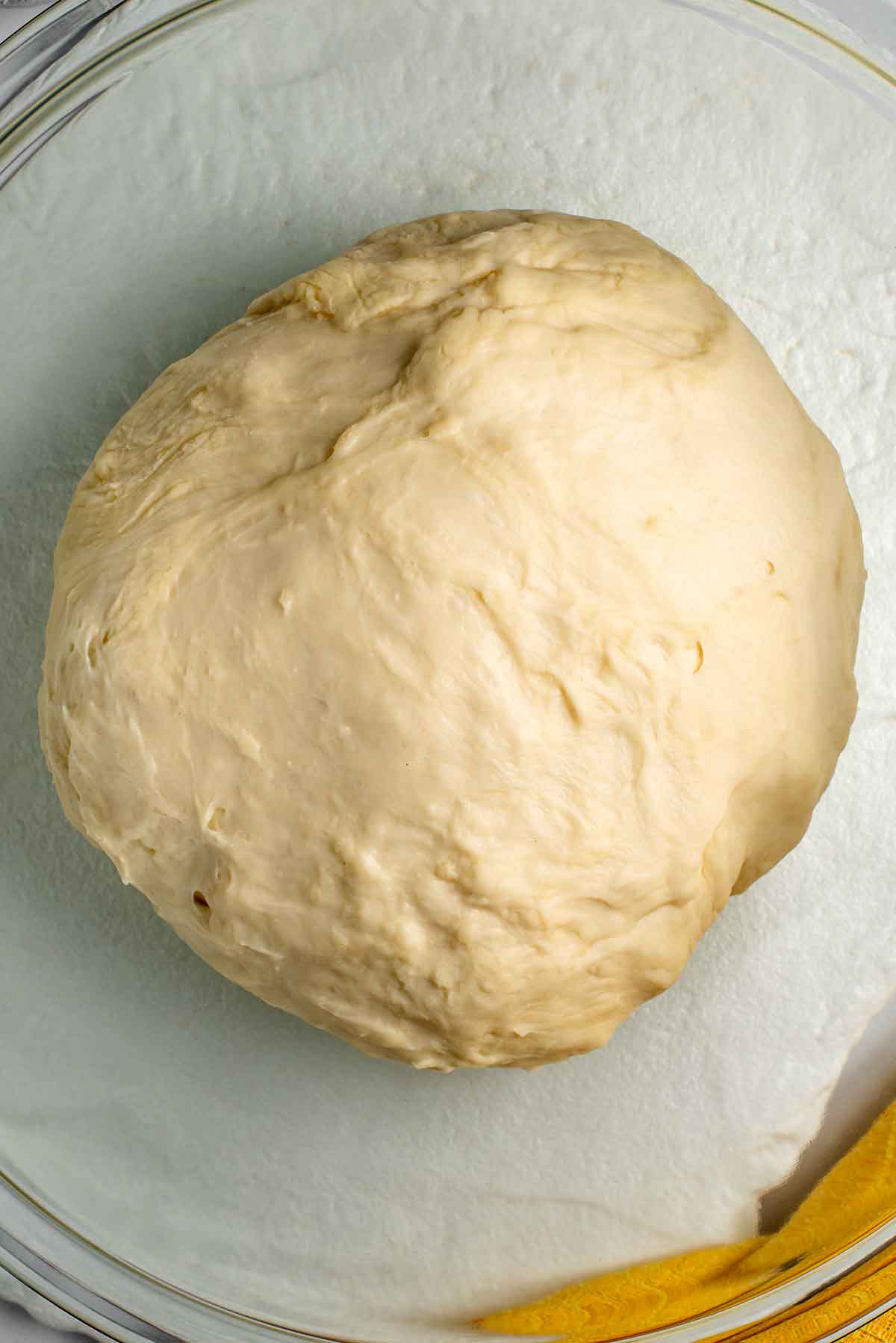Top down view of a soft ball of dough in a large bowl. The dough is quite smooth and not sticky.