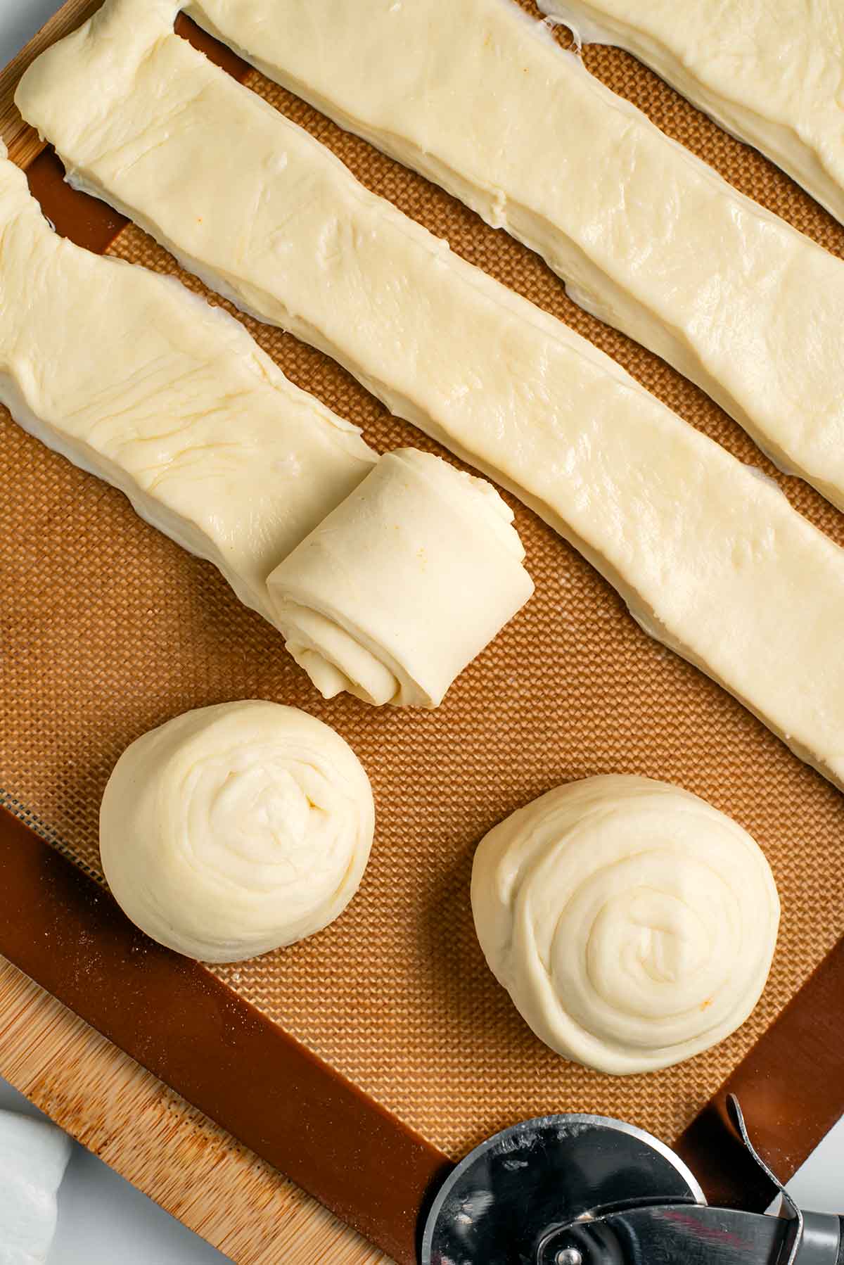 Strips of dough are rolled into a spiralled shape and placed on a silicone baking mat to rest.