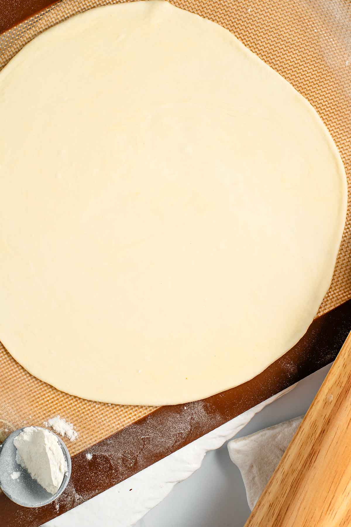 Chapati dough is rolled into a flat circular shape about 8 inches in diameter. The surface underneath the rolled out chapati is lightly floured.