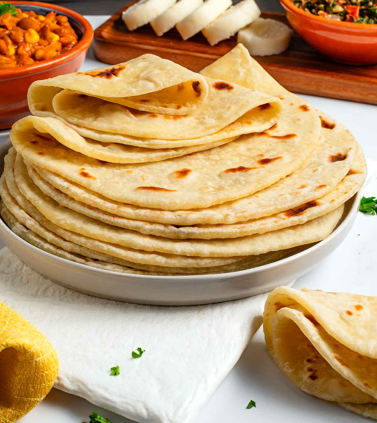 Side view of soft and fluffy Kenyan chapati stacked on a plate. The top chapati is folded to demonstrate its pliability.